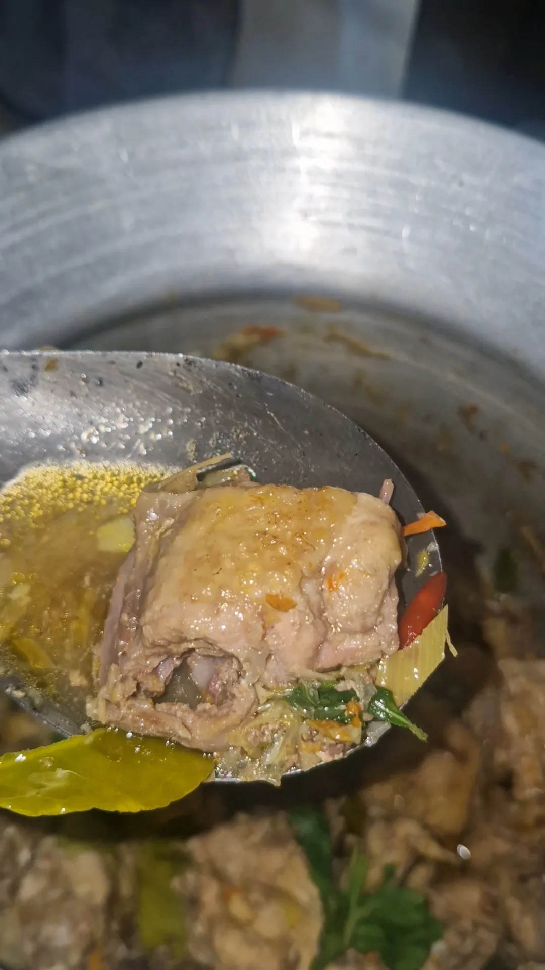ชิ้นไก่ใต้น้ำตักขึ้นในทัพพีพร้อมน้ำจากหม้อและสมุนไพร